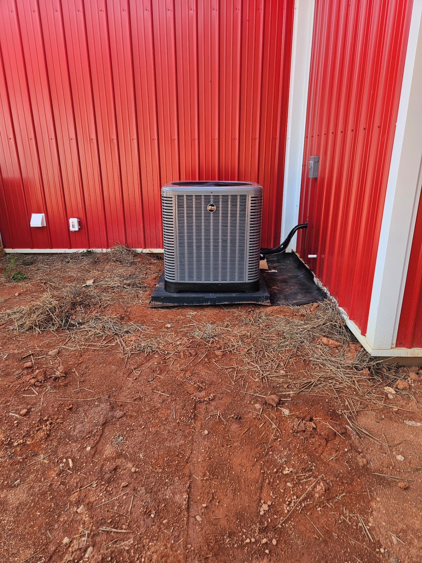Rheem outdoor HVAC unit on a pad beside a red metal building