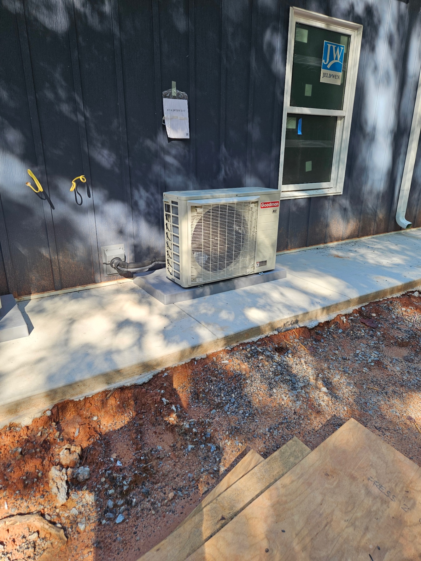 Compact Goodman outdoor HVAC unit beside a building with dark siding